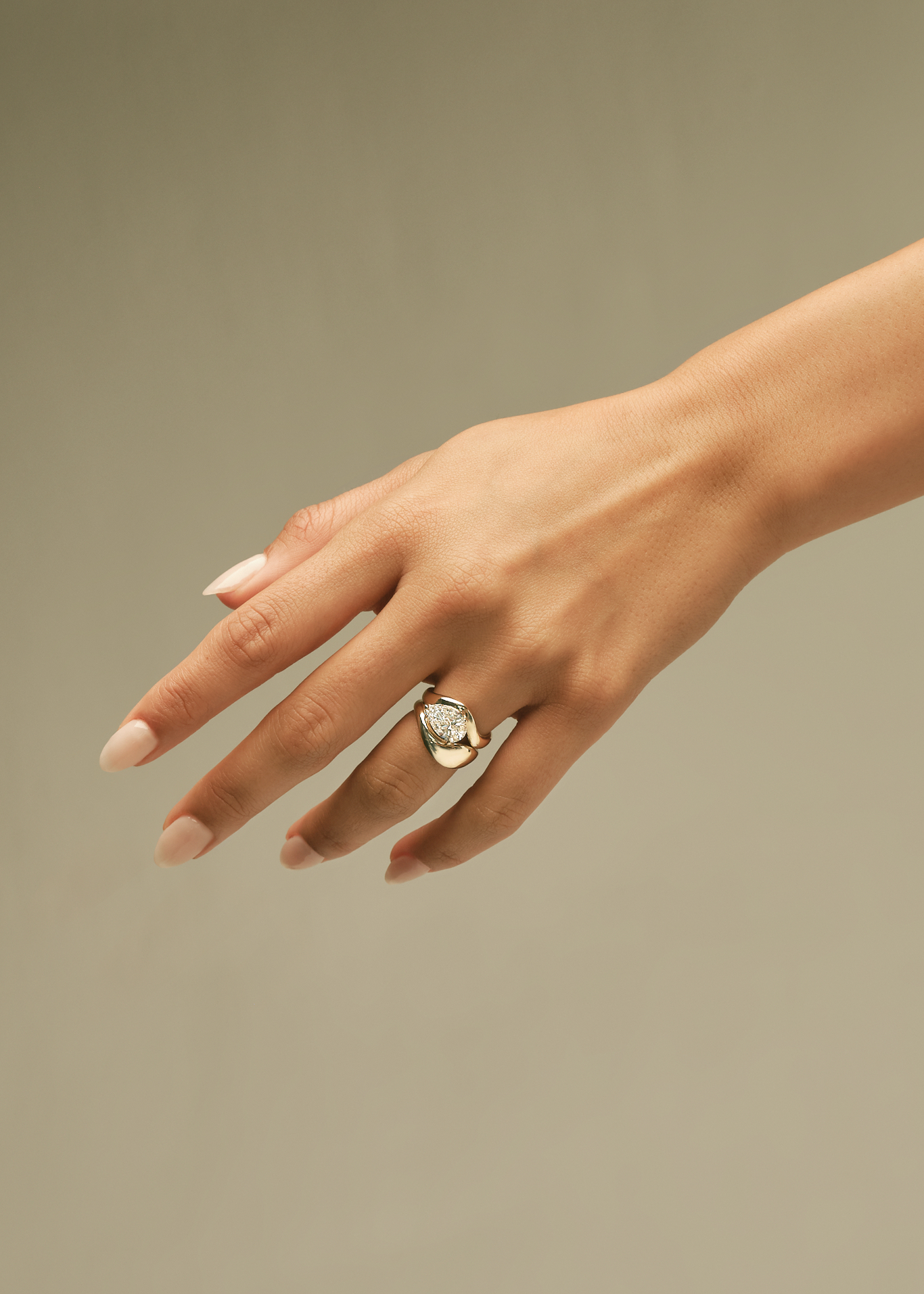 woman's raised hand wearing a Kinn 14k Gold Bold Rosewood Curved Stacking Ring stacked on a Solei Pear Diamond Engagement Ring on her left ring finger