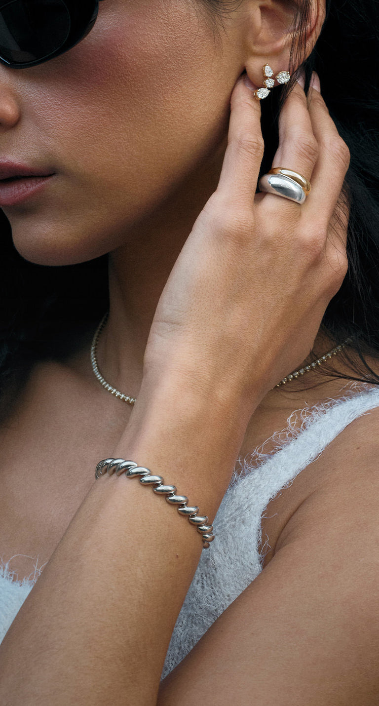 Close-up of a woman's hand with Kinn 14k gold and 925 sterling silver jewelry, including a hampshire house bracelet and dome ring, wearing sunglasses and a white top.
