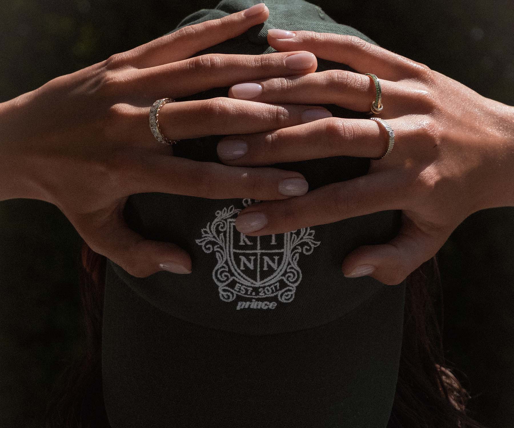 Woman with hands raised to her head wearing a Jane Radiant Diamond Eternity Ring on one hand and a Kinn x Prince 14k Gold Lesley Linked Emerald Ring and Petite Solis RIbbed Diamond Ring on the other hand
