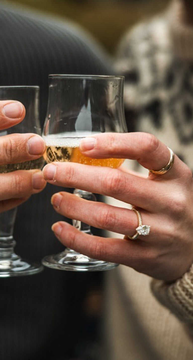 Close up of Bethany's custom diamond engagement ring while clinking glasses