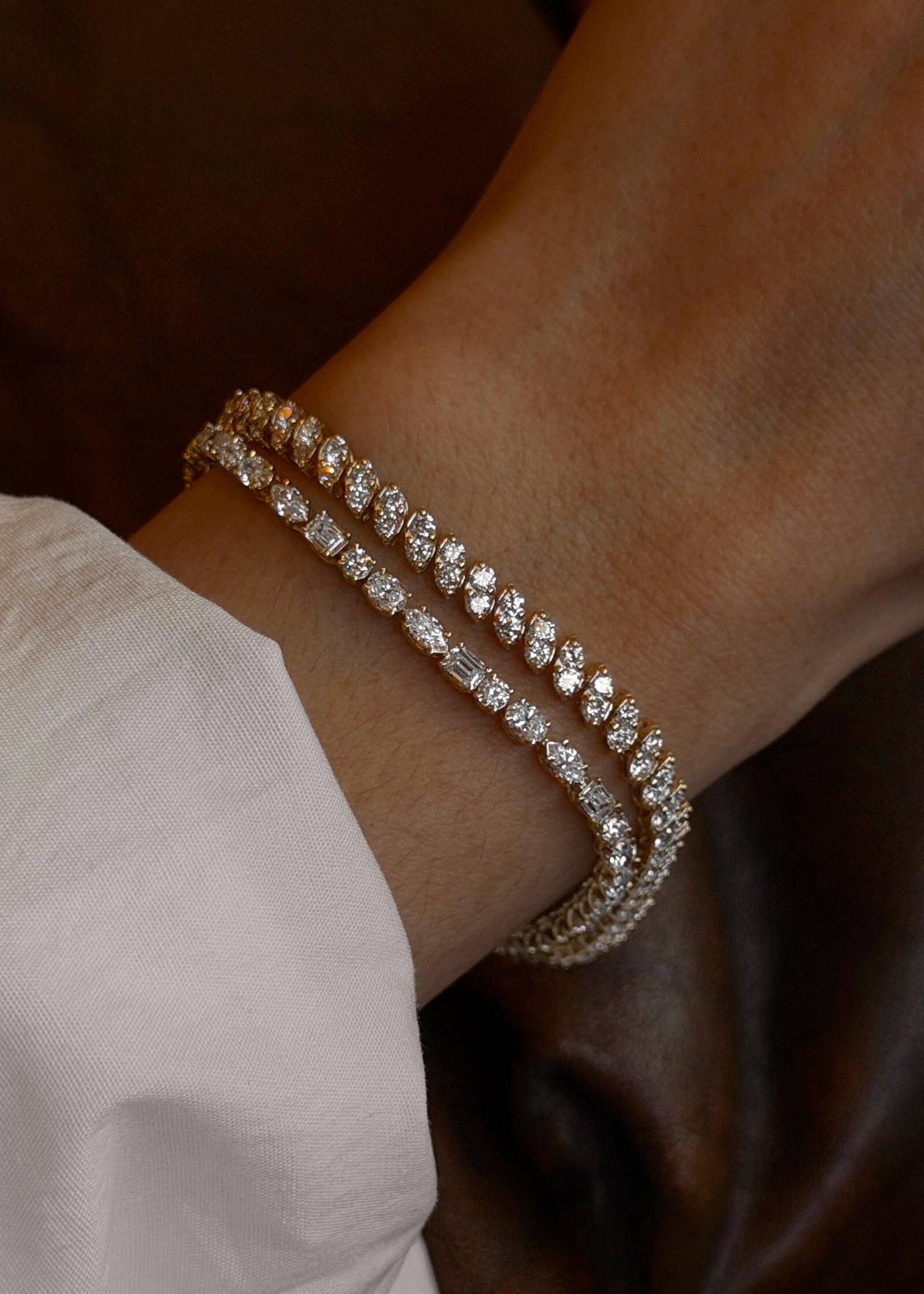 Close-up of a woman's wrist wearing a Kinn 14k gold Esme fancy cut diamond bracelet and a Sofia Marquise Diamond Tennis Bracelet stacked together