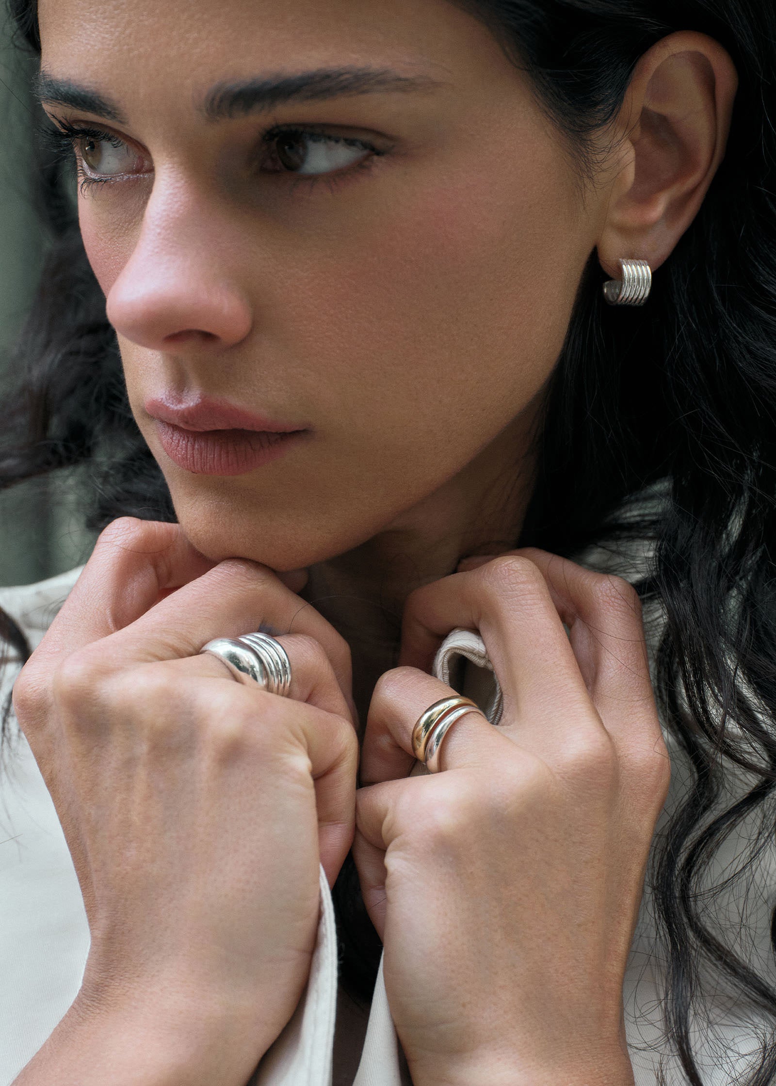 a woman wearing Kinn Studio 925 Sterling Silver Mercer Cuff Hoop Earrings along with bold sterling silver and 14k gold rings stacked on her fingers