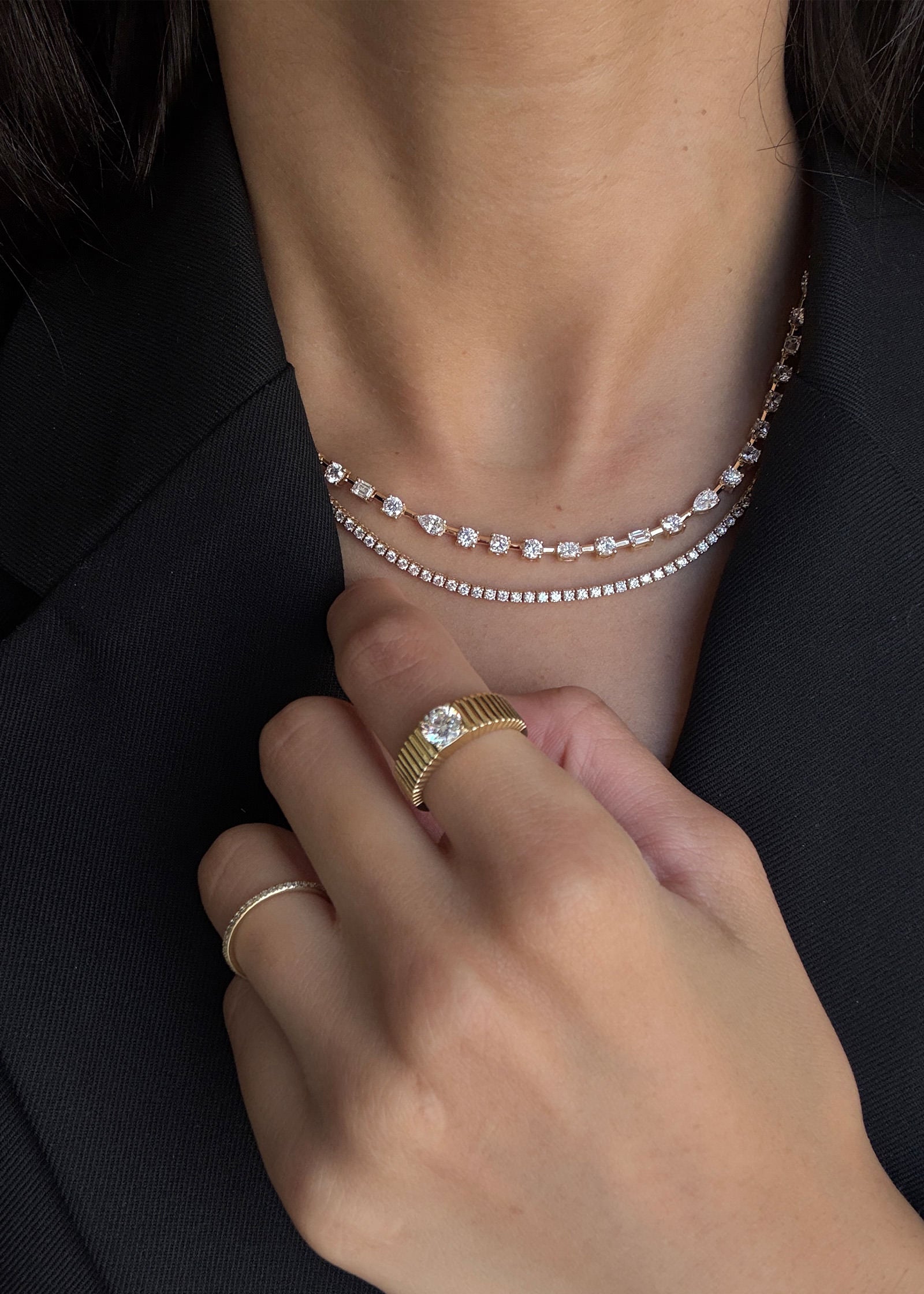 woman in a black blazer wearing a Kinn 14k Yellow Gold Amara Fancy Shape Diamond Tennis Necklace layered with a Diana Diamond Tennis Necklace and wearing a Solis Ribbed Round Diamond 1.0ct Ring on her index finger