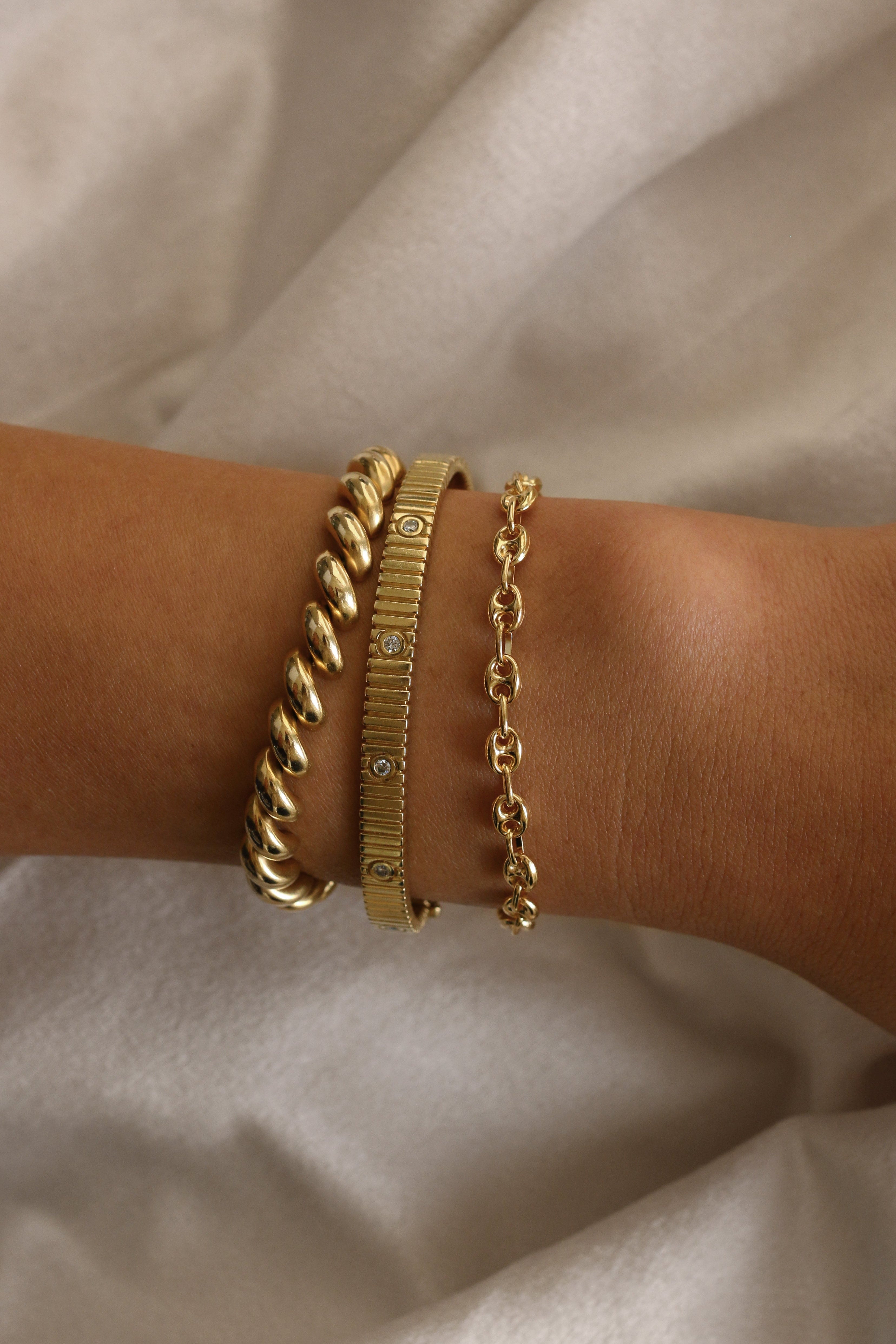 woman's wrist wearing a Kinn 14k Gold Petite Puffed Mariner Chain Bracelet stacked with a Hampshire House Bracelet and a Solis Ribbed IV Anniversary Bracelet