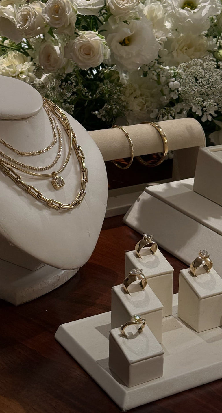Jewelry display with Kinn studio 14k gold  and diamond necklaces and rings with flowers in the back