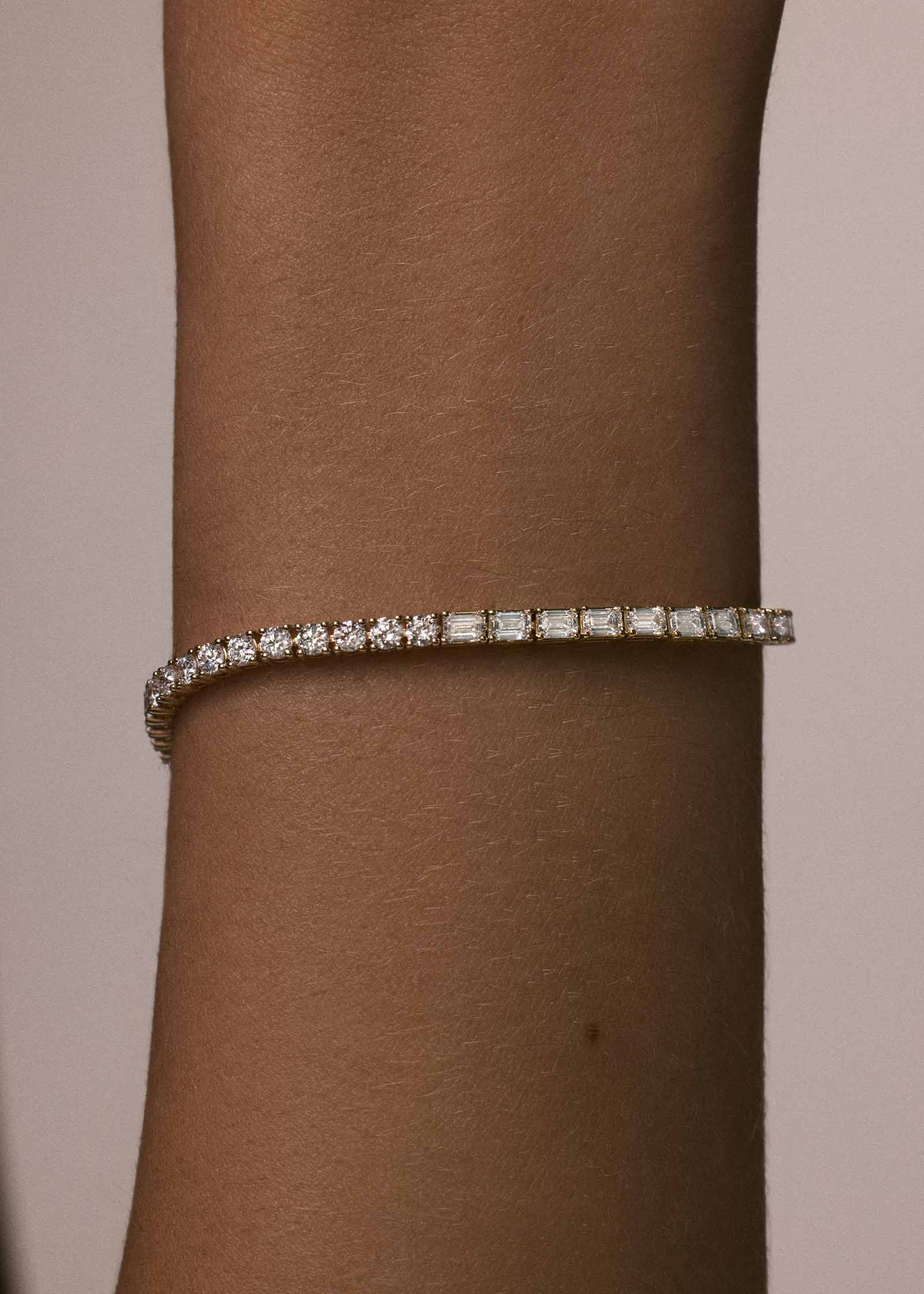 close up of a woman's wrist wearing a Kinn x Prince 14k Gold Billie Half Round Emerald Tennis Bracelet