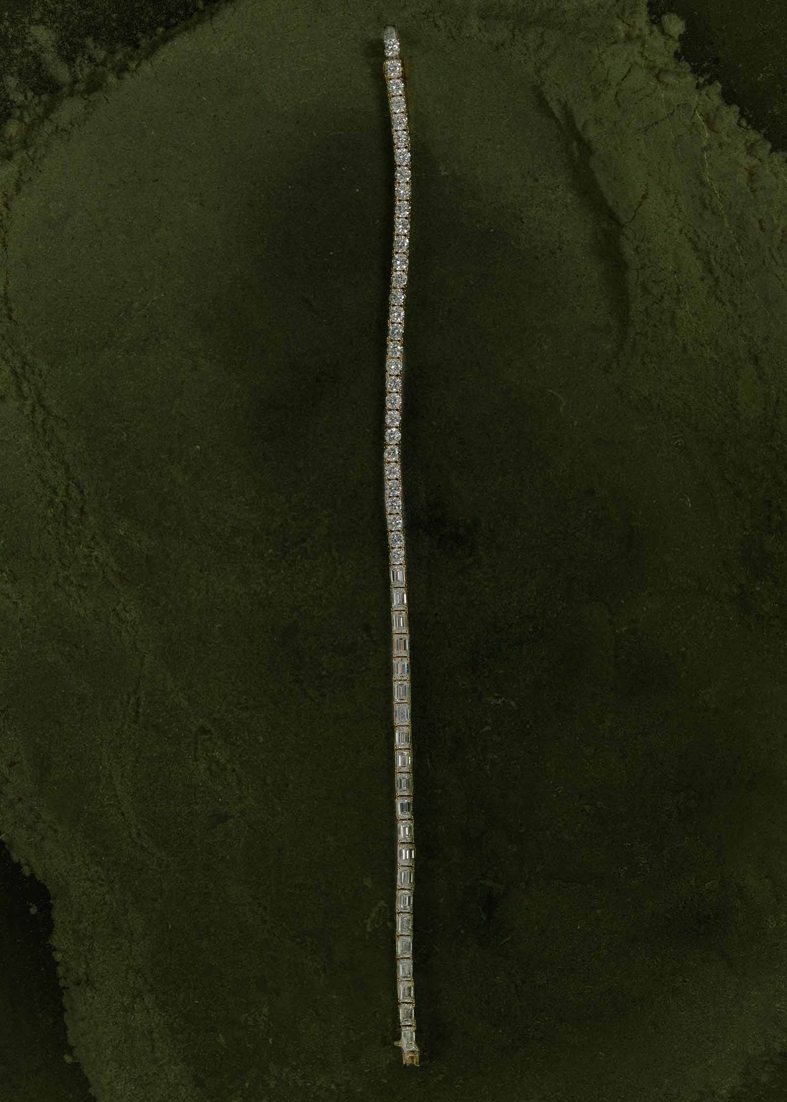 A Kinn x Prince 14k Gold Billie Half Round Emerald Tennis Bracelet laying flat against a green background