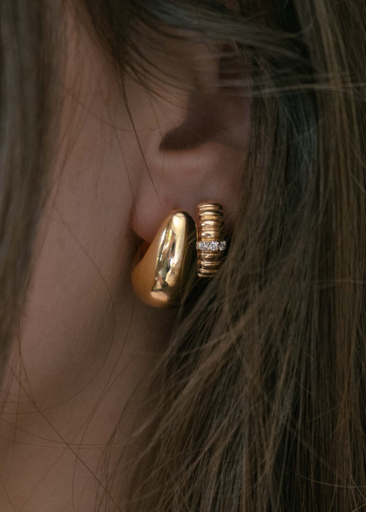 close up of a woman's ear wearing a Kinn 14k Gold Bold Teardrop Hoop Earrings layered with a Solis Ribbed 3 Diamond Huggie in her second piercing