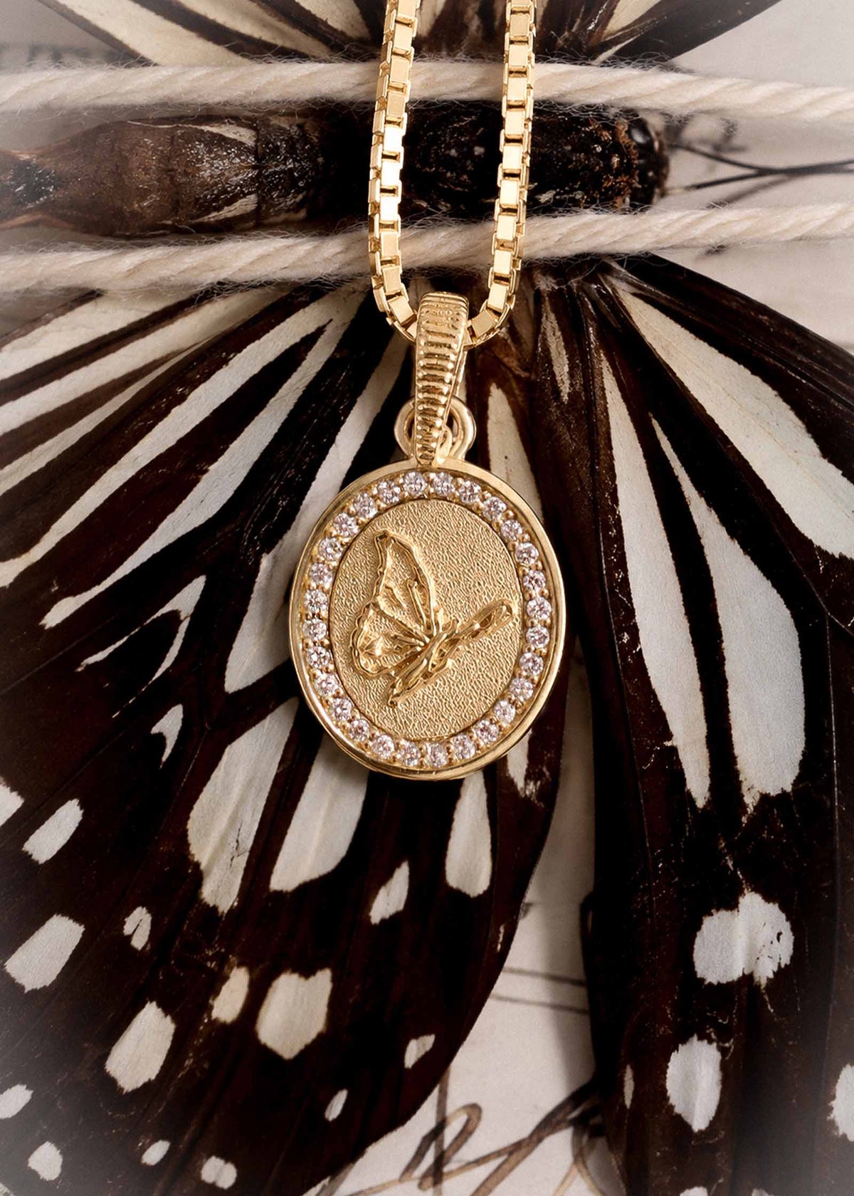 A Kinn 14k Gold Butterfly Dream Diamond Pendant hanging from a gold box chain against a black and white butterfly wing backdrop.
