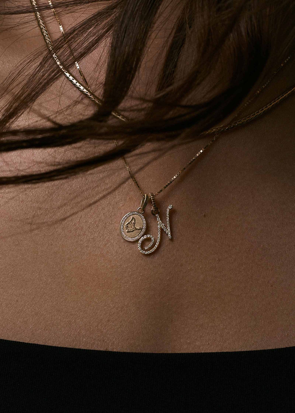 A woman wearing a Kinn 14k Gold Butterfly Dream Diamond Pendant and Pave Diamond Love Letter N Pendant on a box chain necklace
