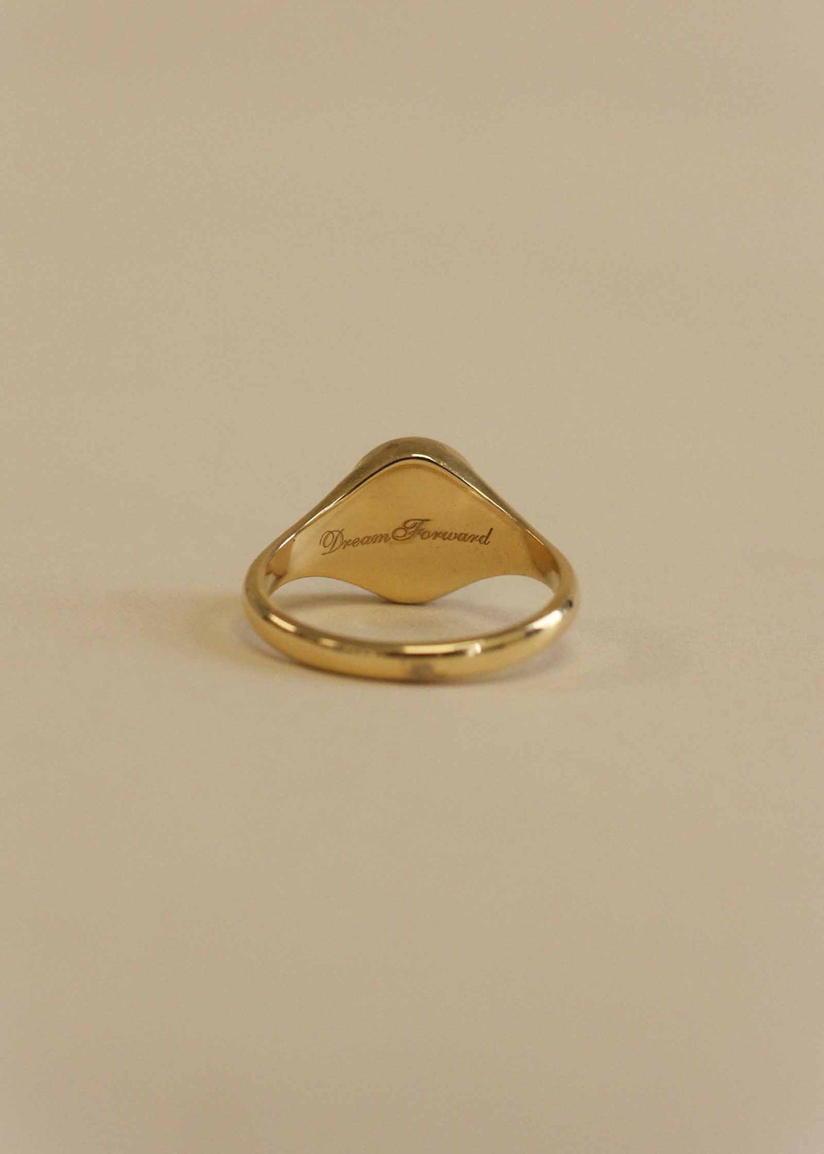 A Kinn 14k Gold Butterfly Dream Signet Ring showing the back of the signet engraved with "Dream Forward" in script font