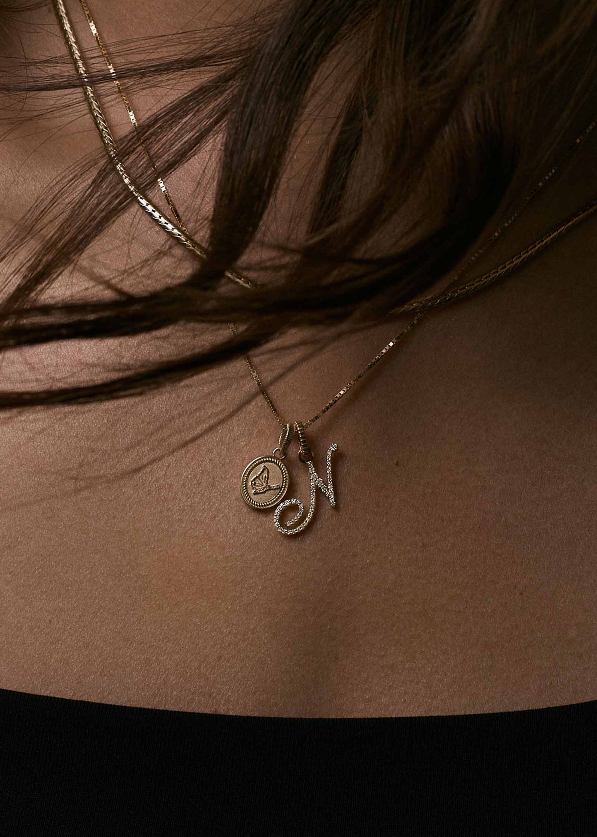A woman wearing a Kinn 14k Gold Butterfly Dream Pendant Necklace with a Pave Love Letter Pendant