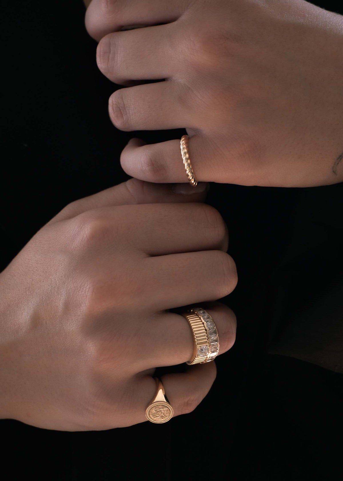 Two hands with one wearing a Kinn 14k Gold Claudine Twist Ring on her pinky and a Solis Ribbed Ring Round Diamond 0.5 Carat stacked with a Jane Eternity Band on her other hand with a Pegasus Dream Signet Ring on the pinky