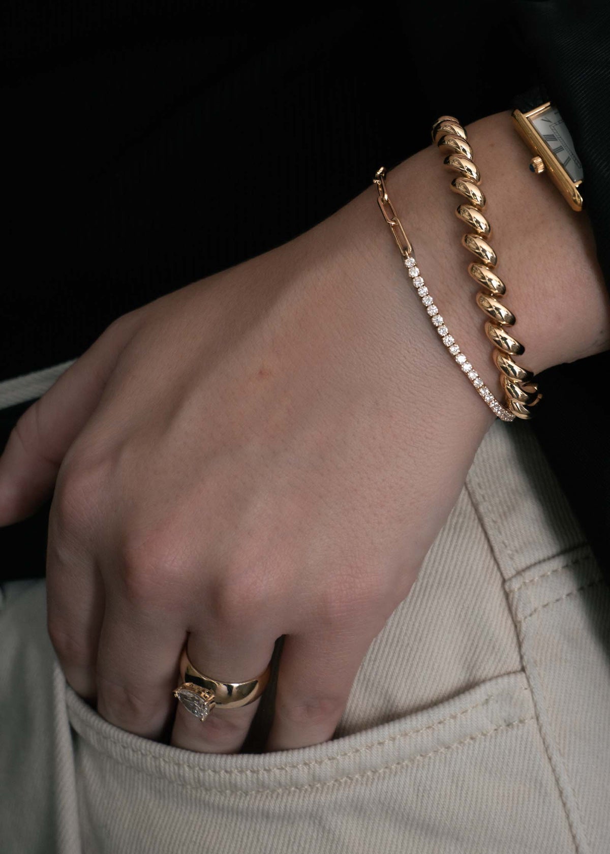 woman wearing a Kinn Studio 14k Gold Coco Round Diamond Tennis Link Bracelet stacked with a Hampshire House Bracelet and vintage watch with her hand tucked into her pocket