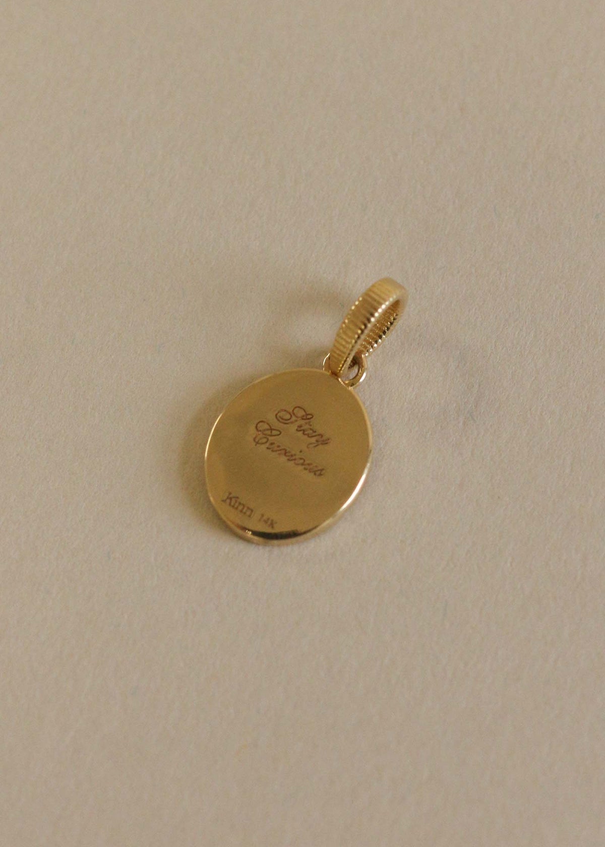 A Kinn 14k Gold Crescent Dream Diamond Pendant laying flat showing the back side engraved with "Stay Curious" in script font