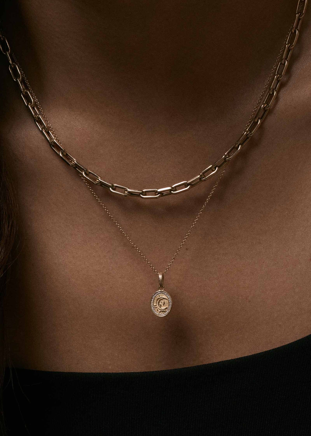A close-up of a woman wearing a Kinn 14k Gold Crescent Dream Diamond Pendant on a micro rolo chain necklace layered with a Mia Link Chain Necklace