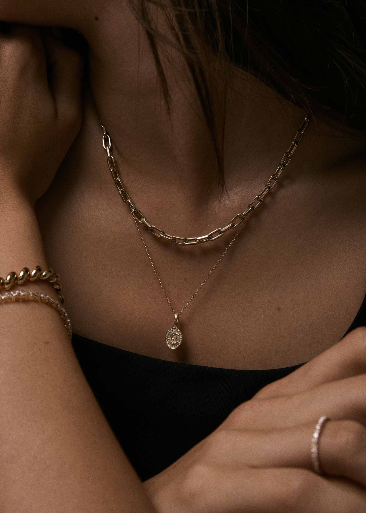 A close-up of a woman wearing a Kinn 14k Gold Crescent Dream Diamond Pendant on a micro rolo chain necklace layered with a Mia Link Chain Necklace
