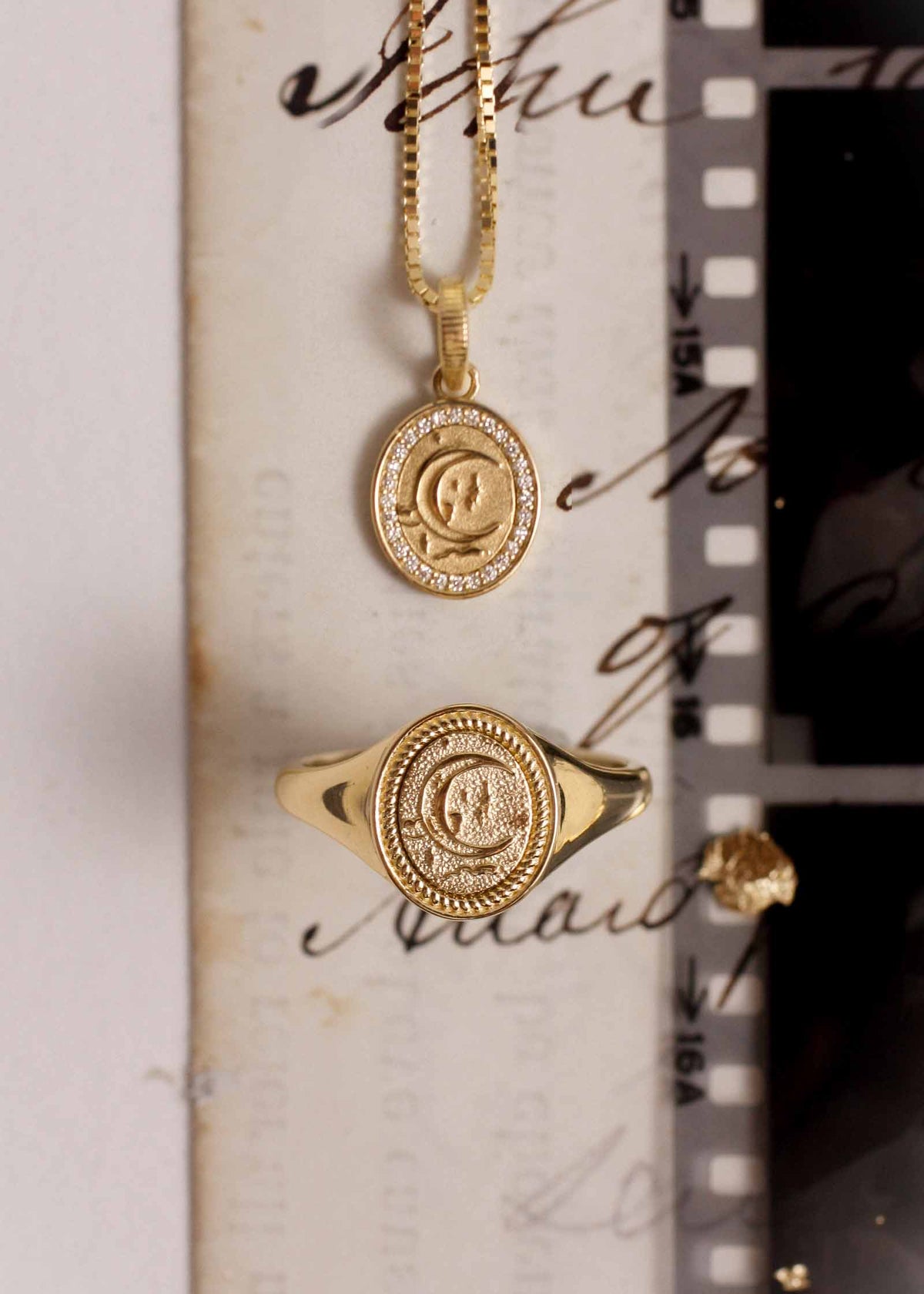 A Kinn 14k Gold Crescent Dream Signet Ring laying flat with a Crescent Dream Diamond Pendant Necklace against a note
