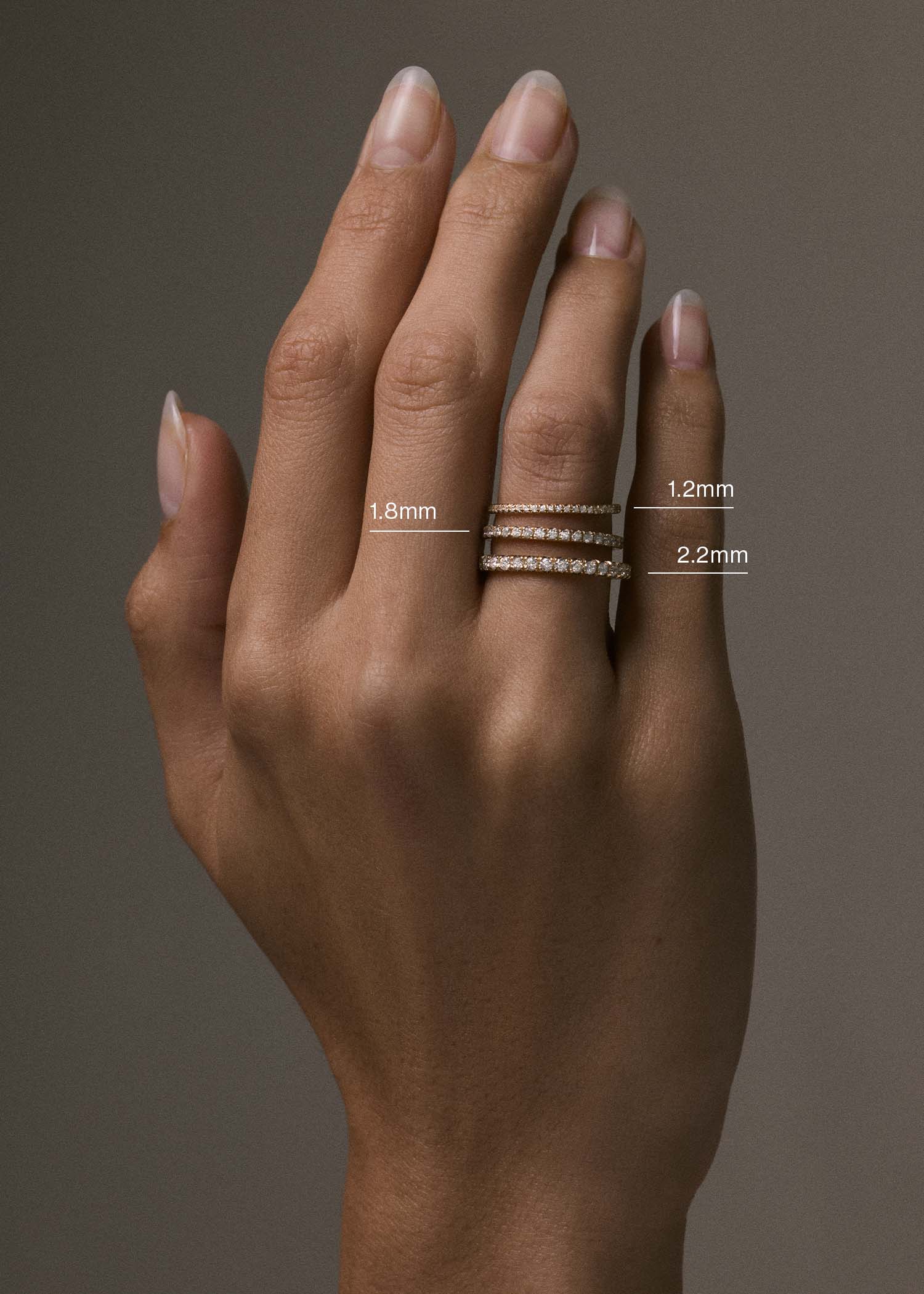 A raised hand wearing 3 different band widths of the Kinn 14k Gold Dahlia Pavé Diamond Band Ring in 1.2mm, 1.8mm, and 2.2mm