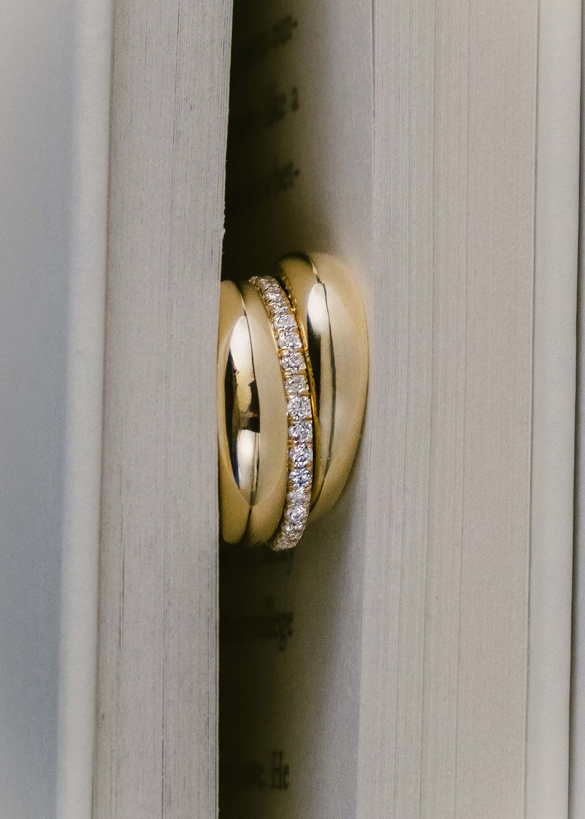 Two Kinn 14k Gold Dare To Love Classic Dome Rings with a Dahlia Pave Diamond Eternity Ring stacked together and wedged in between the pages of a book