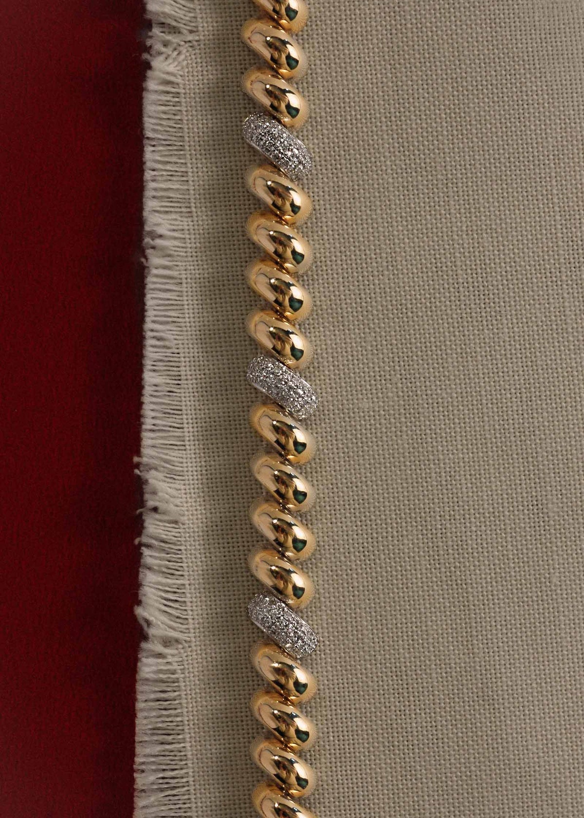 A Kinn 14k Gold Pavé Diamond Petite Hampshire House Bracelet laying flat on a piece of fabric against a dark red background