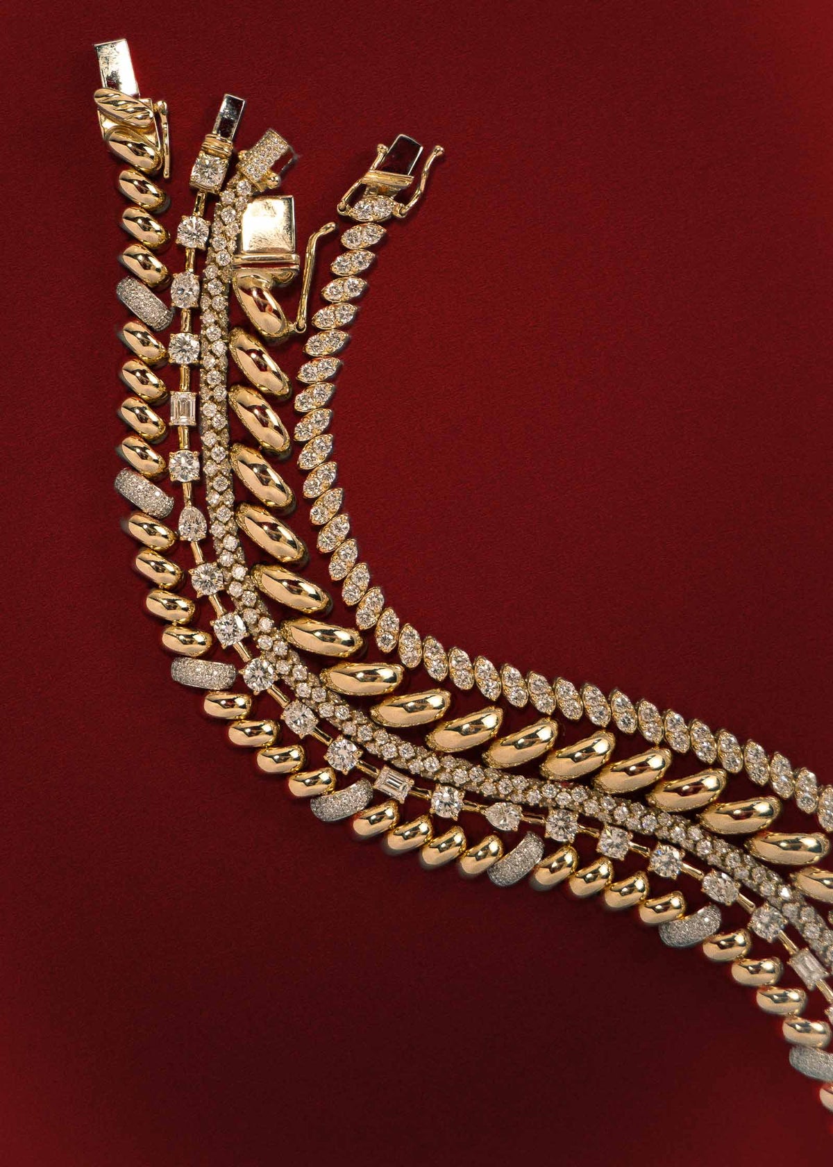 A Kinn 14k Gold Pavé Diamond Petite Hampshire House Bracelet laying flat in a curved manner next to an Amara bracelet, Isadora Tubular Diamond Tennis Bracelet, Hampshire House Bracelet, and Sofia Marquise Diamond Bracelet against a dark red background