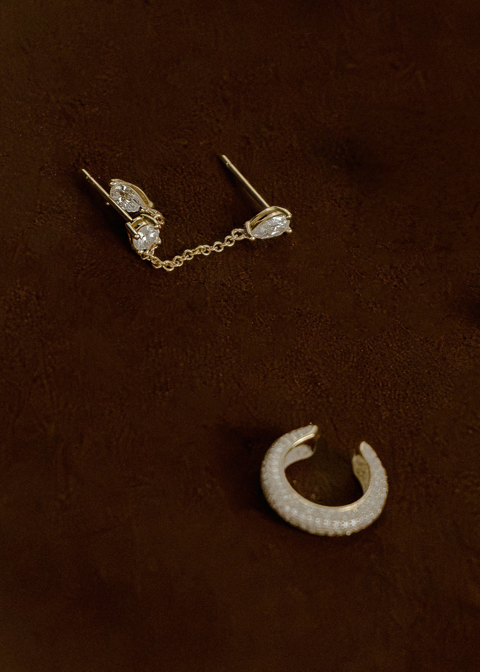 A Kinn x Prince 14k Gold Doubles Diamond Chain Earring and a Love Pave Diamond Ear Cuff laying on its side against a clay background