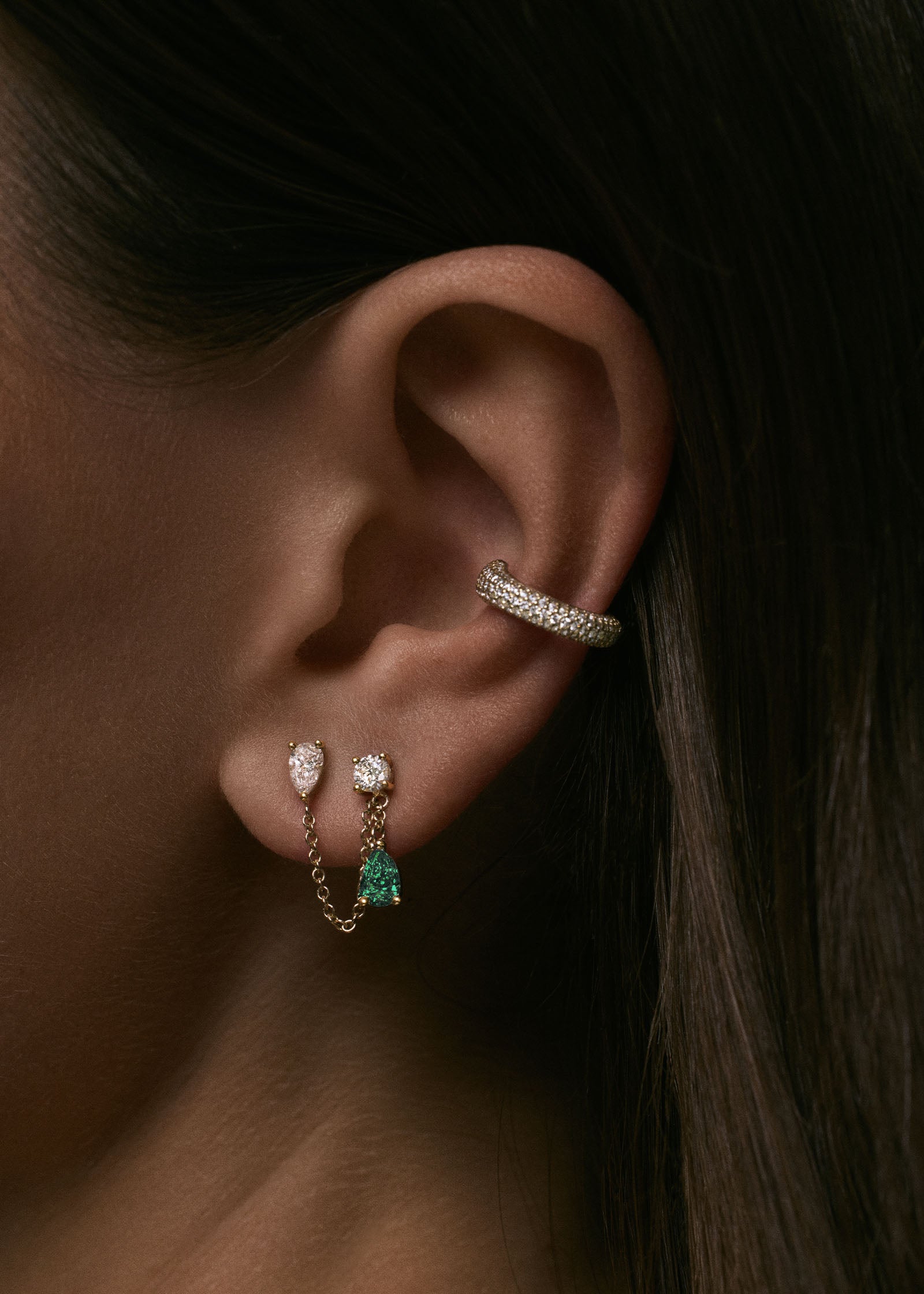 A close up of a woman's ear wearing a Kinn x Prince 14k Gold Doubles Diamond & Emerald Chain Earring paired with a Love Pavé Diamond Ear Cuff