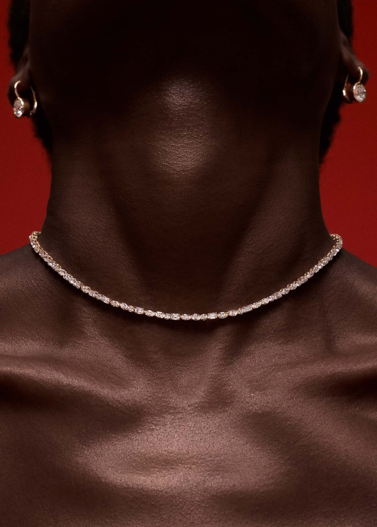 woman with her chin raised wearing a Kinn 14k Yellow Gold Esme Fancy Shape Diamond Tennis Necklace against a red background 
