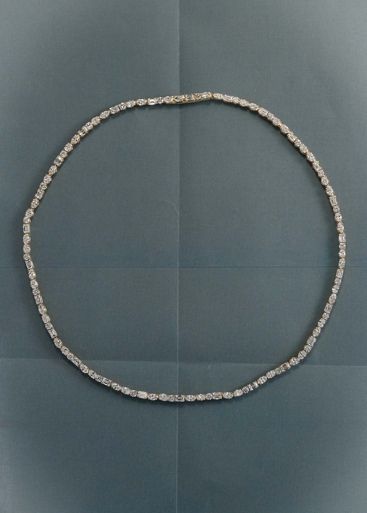 A Kinn 14k Yellow Gold Esme Fancy Shape Diamond Tennis Necklace laying flat against folded blue paper