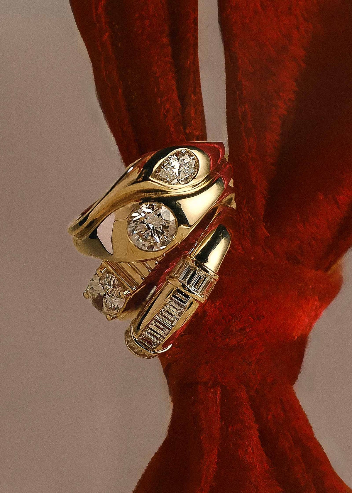 A Kinn 14k Gold Gigi Toi et Moi Diamond Round Pear Ring stacked on a 14k Gold Solis Ribbed Ring Oval Diamond and Beatrice Channel Set Baguette Diamond Ring hanging from a red velvet ribbon