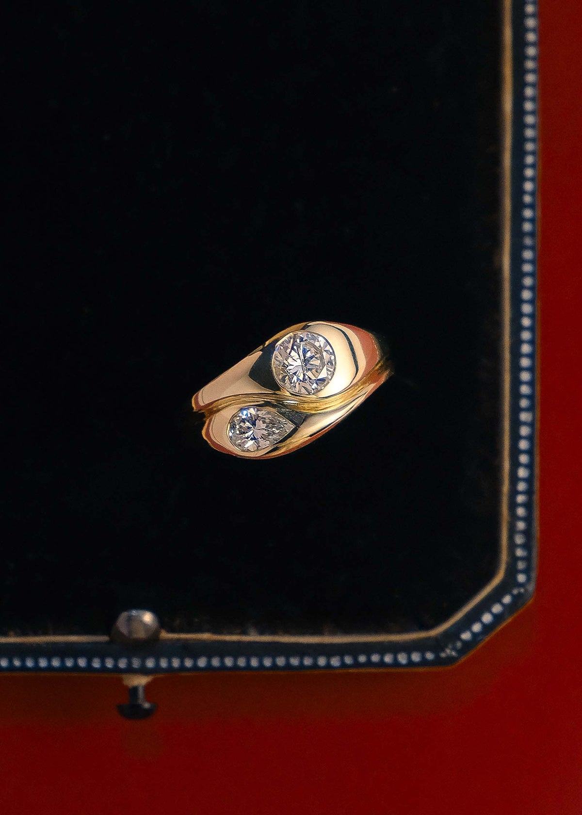 Close up of a Kinn 14k Gold Gigi Toi et Moi Diamond Round Pear Ring laying in a jewelry box against a red background