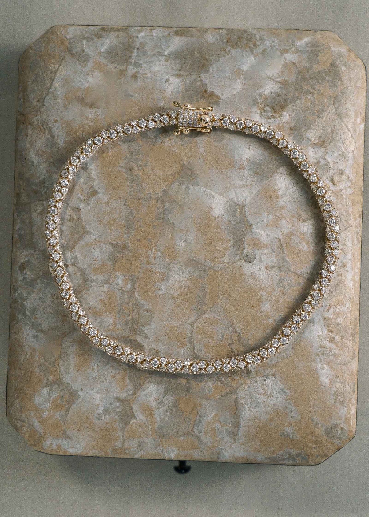 A Kinn 14k Gold Isadora Tubular Diamond Tennis Bracelet laying flat against a stone background