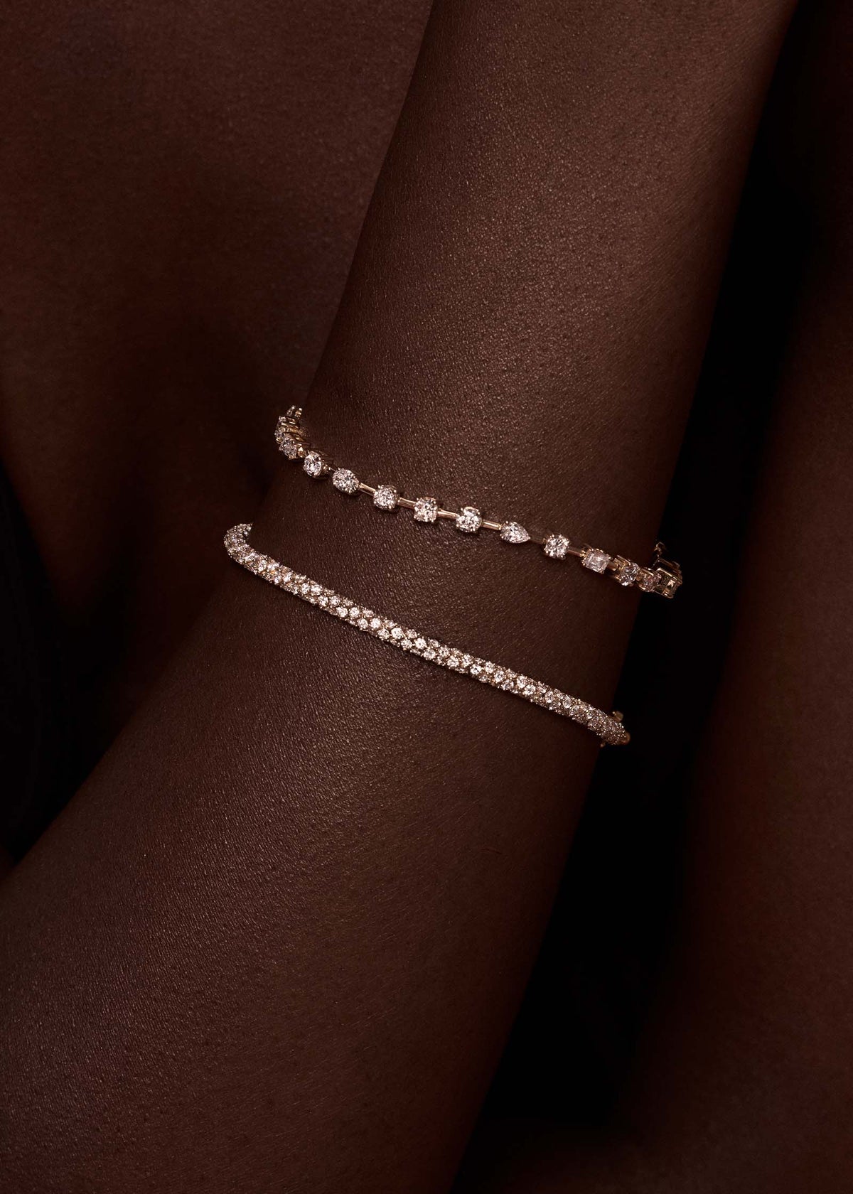 A close up of a woman's arm wearing a Kinn 14k Gold Isadora Tubular Diamond Tennis Bracelet stacked with an Amara Fancy Shape Diamond Tennis Bracelet