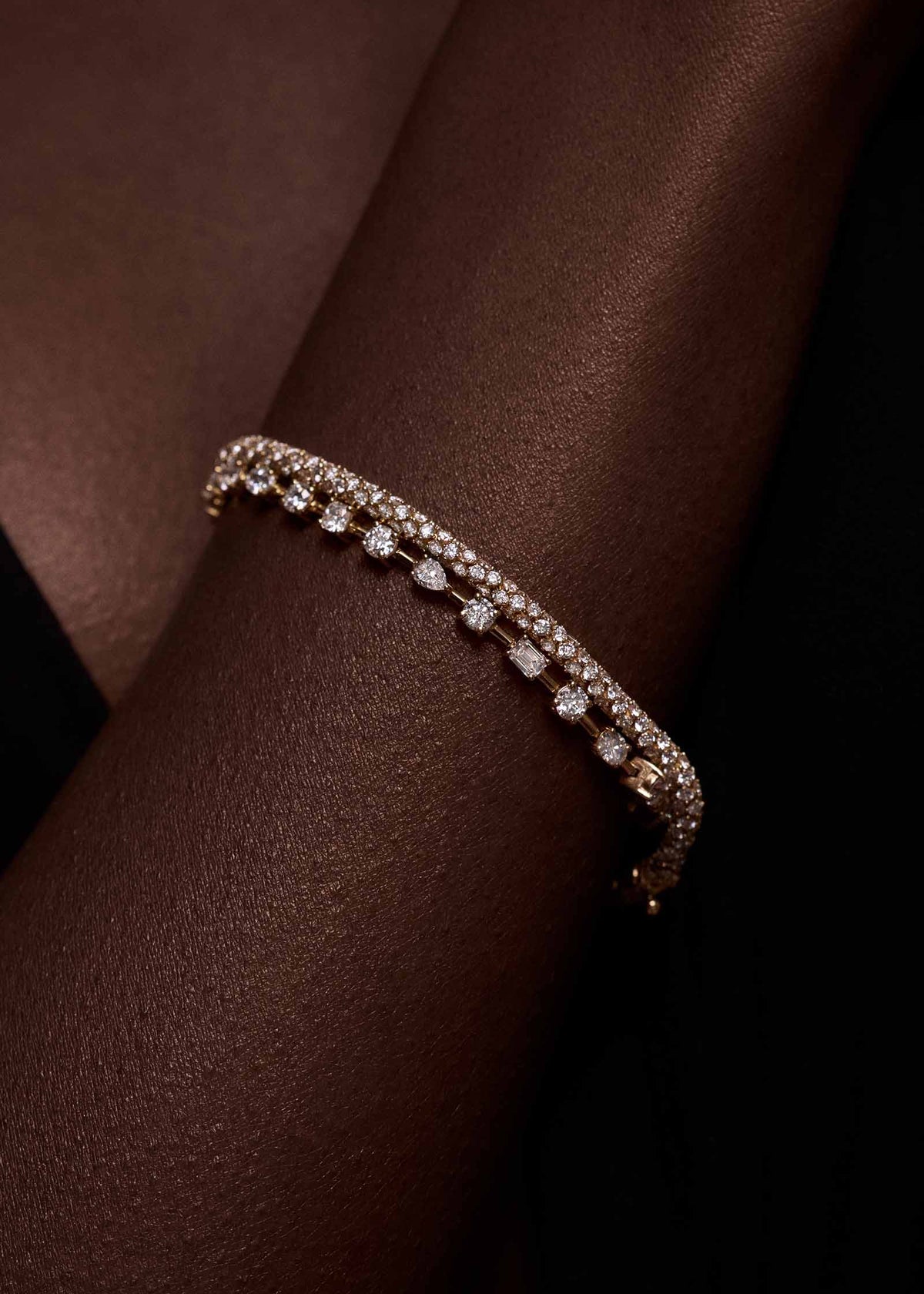 A close up of a woman's arm wearing a Kinn 14k Gold Isadora Tubular Diamond Tennis Bracelet stacked with an Amara Fancy Shape Diamond Tennis Bracelet