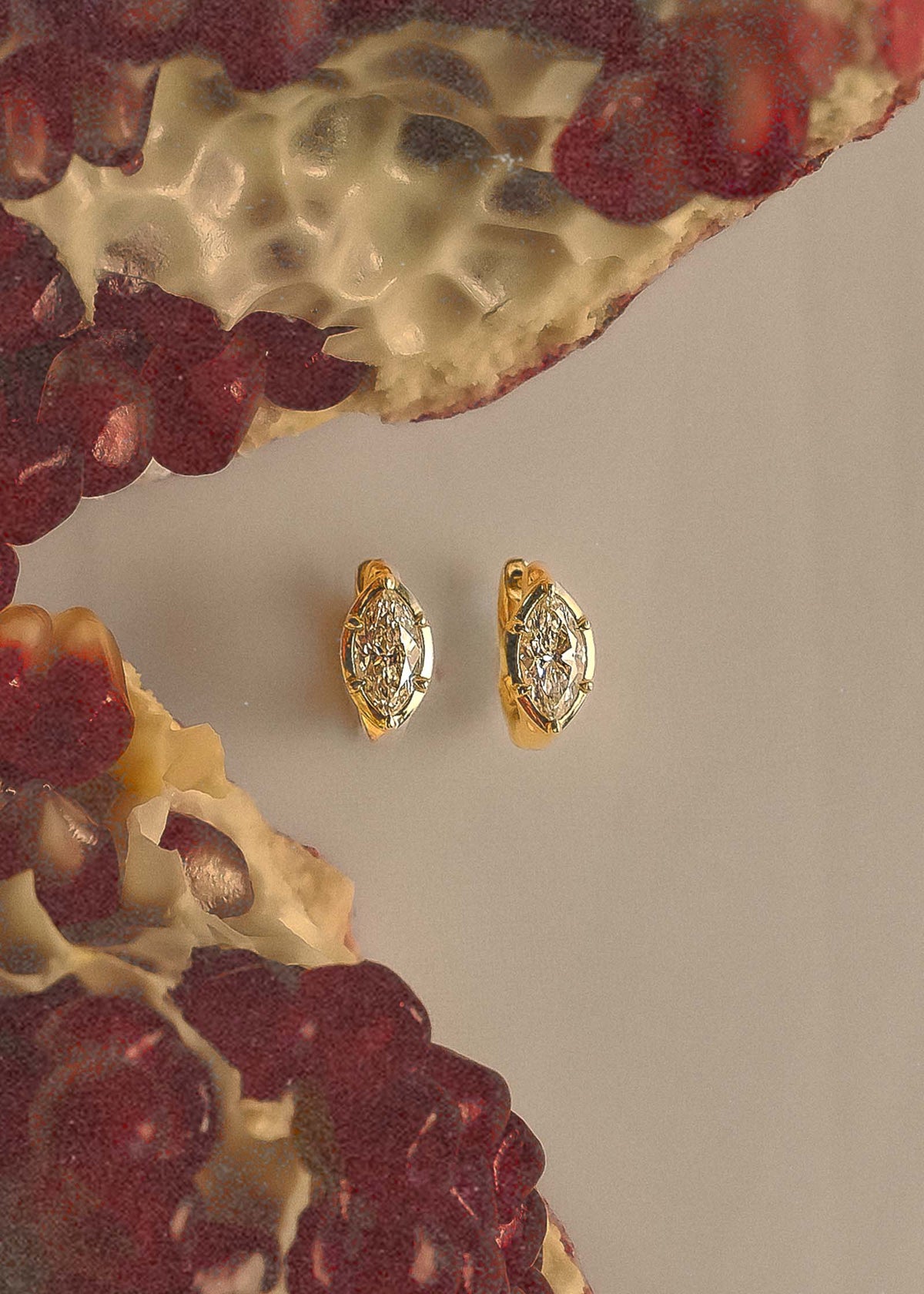A pair of Kinn 14k Gold Jackson Marquise Diamond Huggie Hoop Earrings  sitting next to an open pomegranate