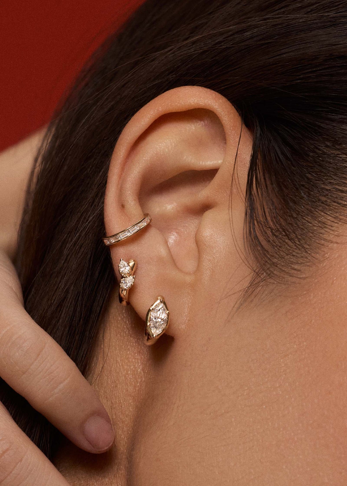close up of a woman's ear wearing a Kinn 14k Gold Jackson Marquise Diamond Huggie Hoop Earring layered with a Double Pear Diamond Huggie and a Bobbi Baguette Ear Cuff