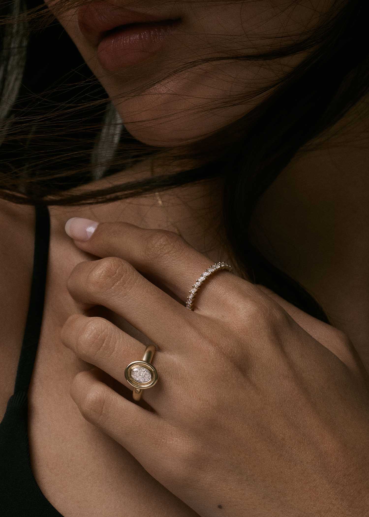 close up of woman's hand wearing a Kinn Studio 14k Gold The Jardin Diamond Engagement Ring on her ring finger and a Petite Marquise Diamond Eternity Band Ring on her index finger