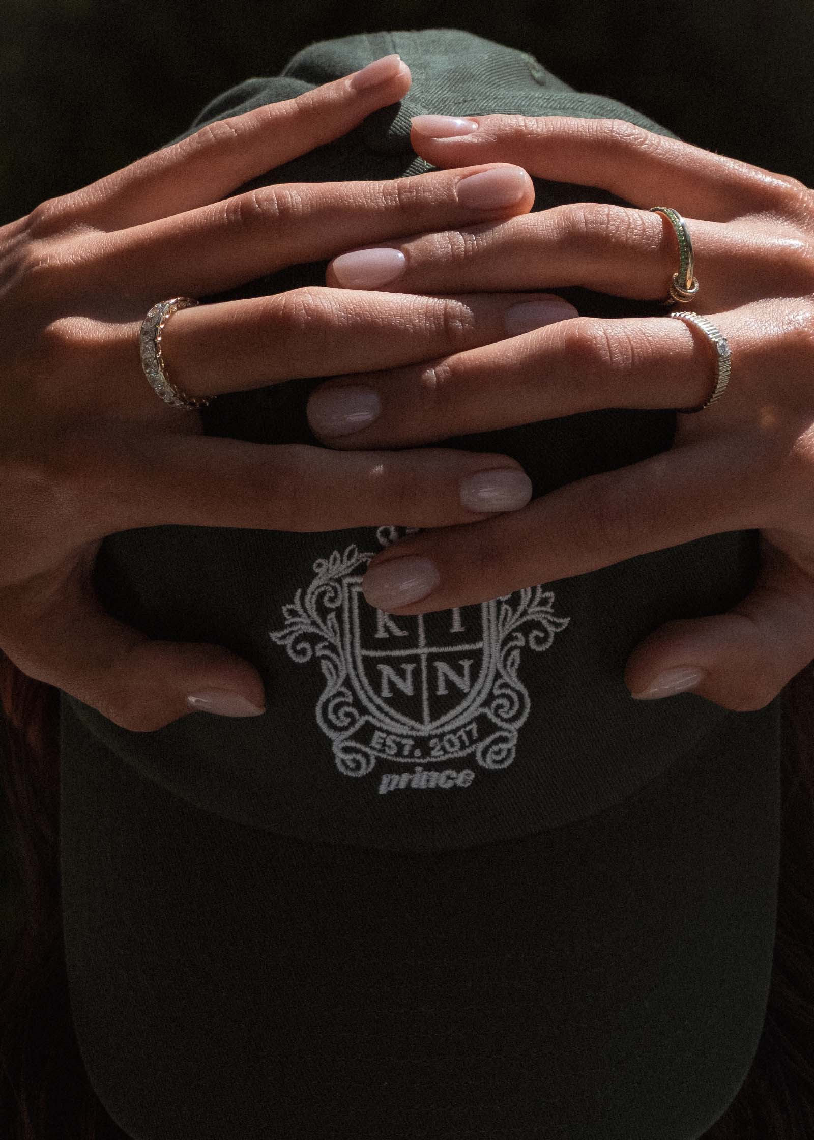 woman with her hands raised to her head wearing Kinn x Prince 14k Gold Lesley Linked Emerald Band Ring, Solis Ribbed Ring, and Jane Radiant Eternity and a Club Cap