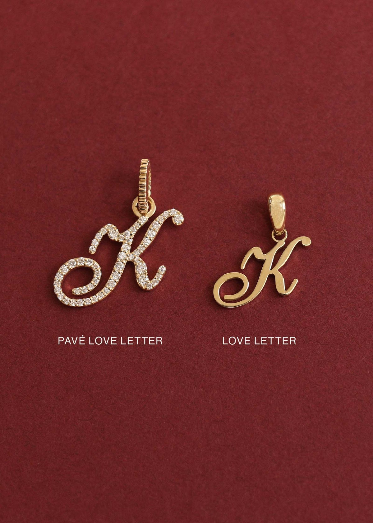 Kinn 14k Gold Pavé Diamond Love Letter "K" Charm Pendant next to a Love Letter Charm "K" laying against a red background to demonstrate the size difference between the two