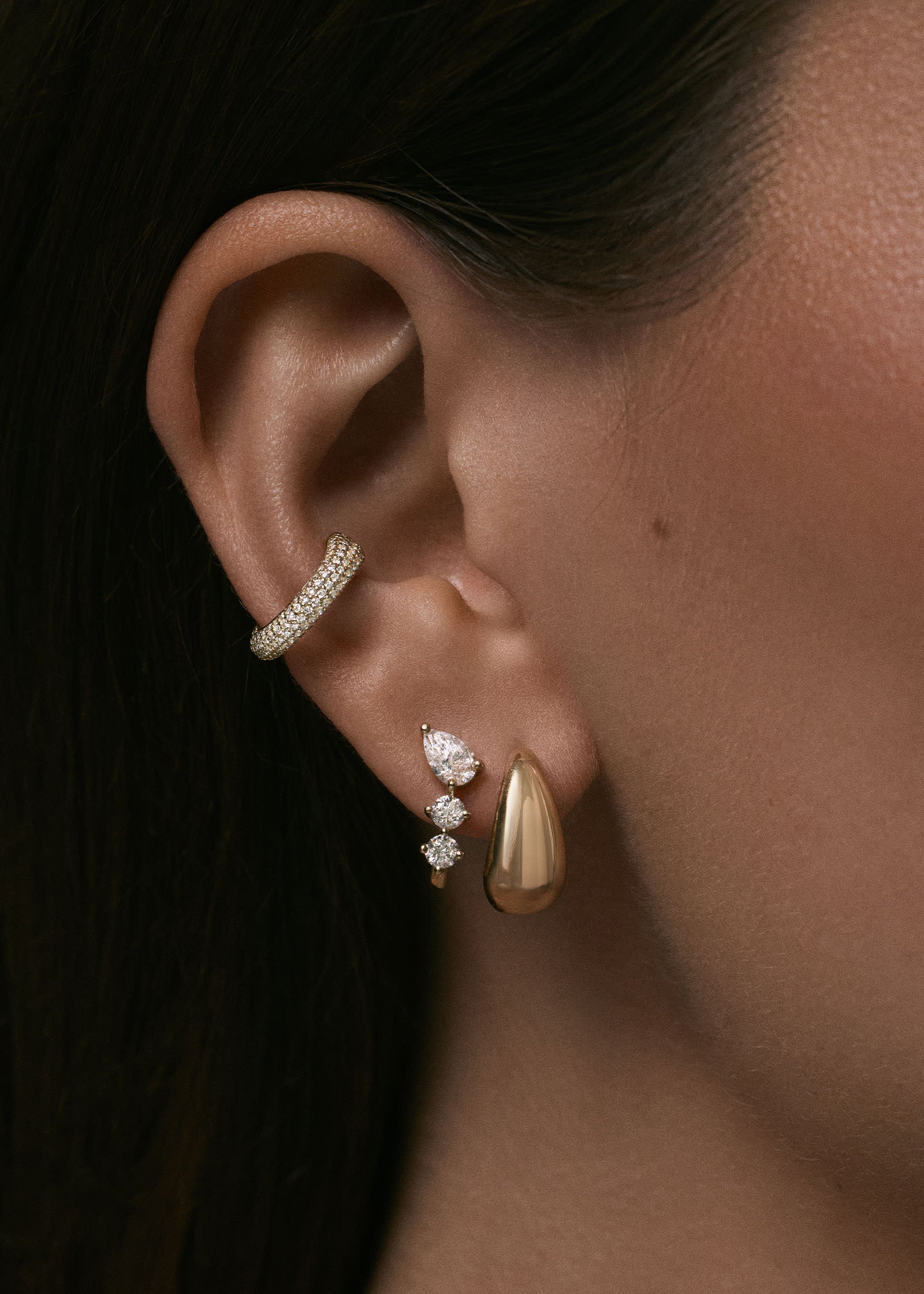 close up of a woman wearing a Kinn x Prince 14k Gold Love Pavé Diamond Earring Cuff layered with a Jules Mixed Diamond J Hoop Earring and a 14k Gold Teardrop Hoop Earring