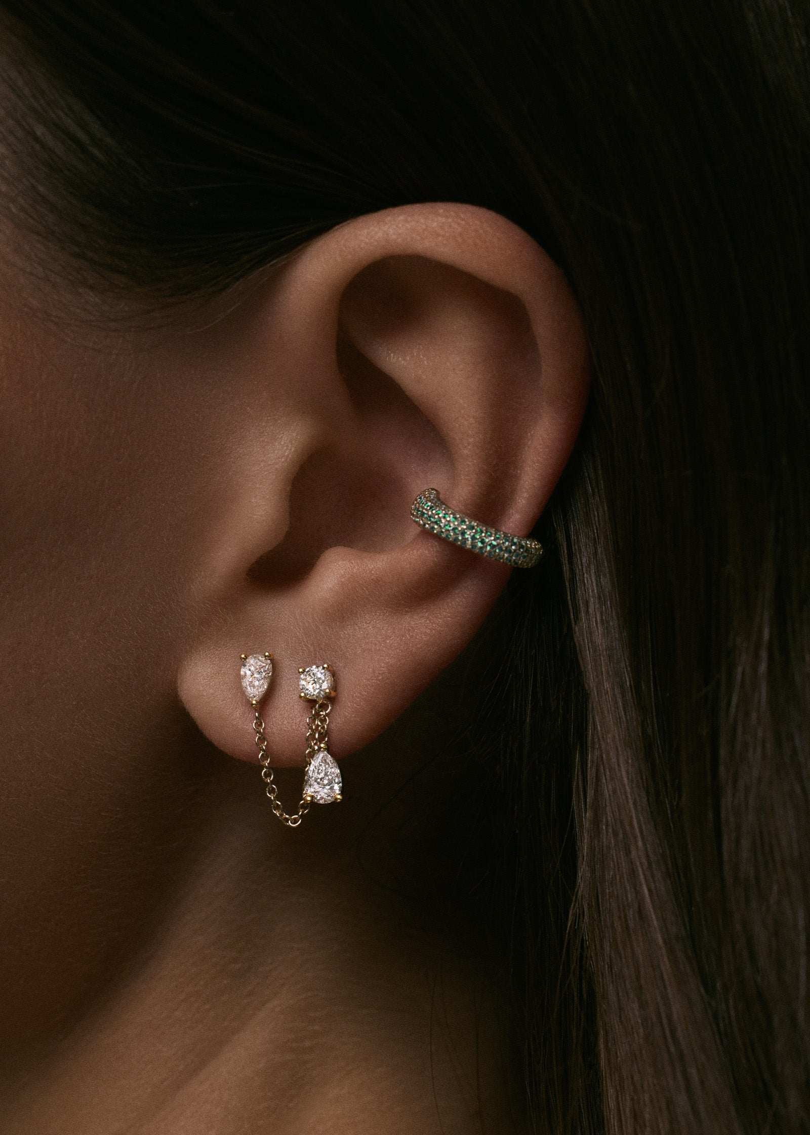 close up of woman wearing a Kinn x Prince 14k Gold Love Pavé Emerald Earring Cuff layered with a Doubles Diamond Chain earring