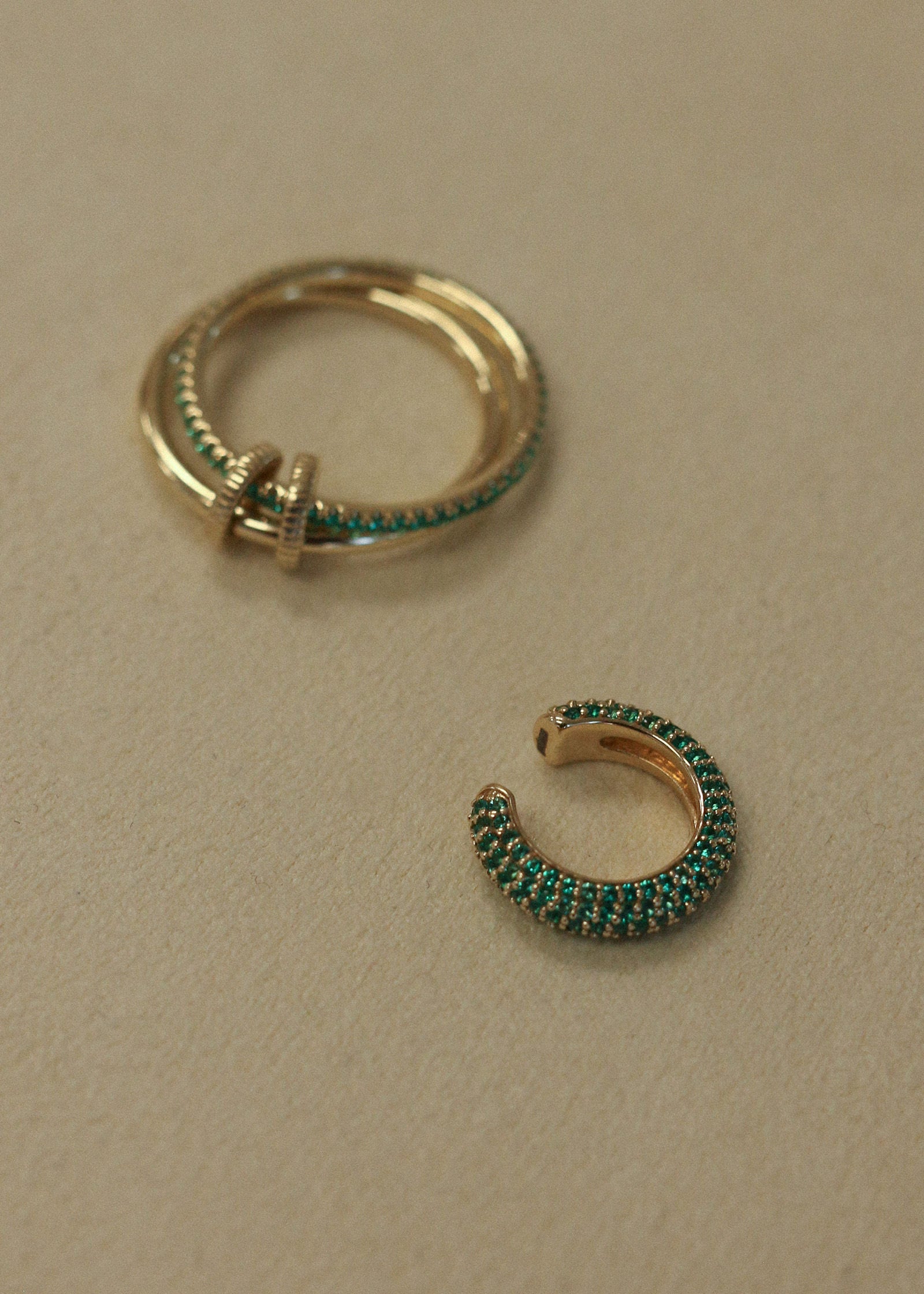 A Kinn x Prince 14k Gold Love Pavé Emerald Earring Cuff laying next to a Lesley Linked Pave Emerald Ring