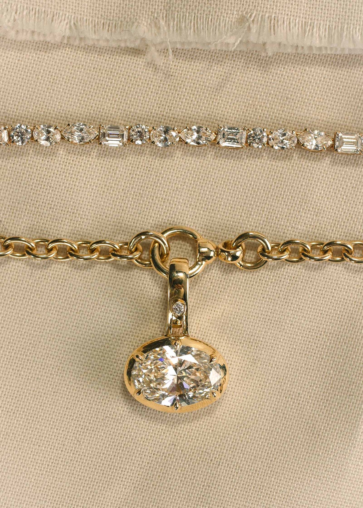 close up of the diamonds on a Kinn 14k Yellow Gold Esme Fancy Shape Diamond Tennis Necklace laying flat next to a Madeleine East West Oval Diamond Pendant