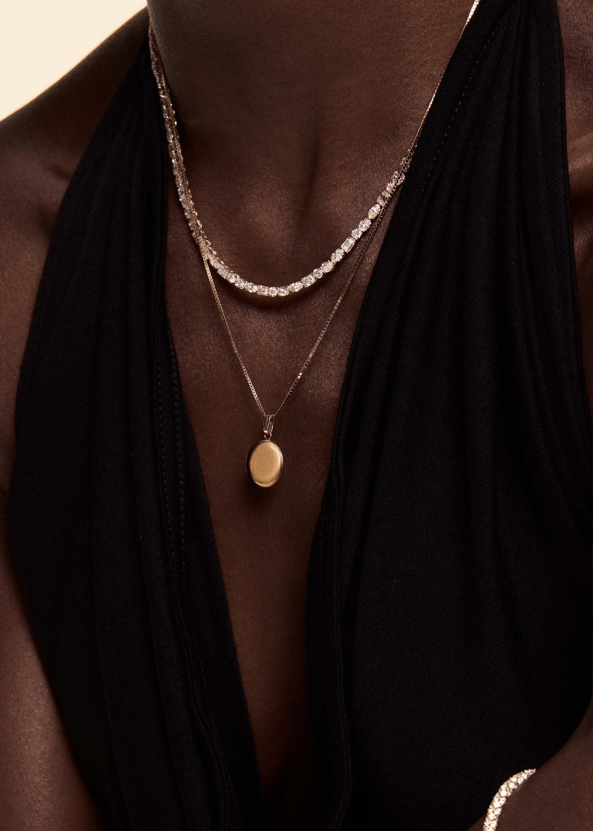 Woman in a black halter top wearing a Kinn 14k Gold Maison Round Locket on a long box chain necklace and layered with an Esme Diamond Tennis Necklace