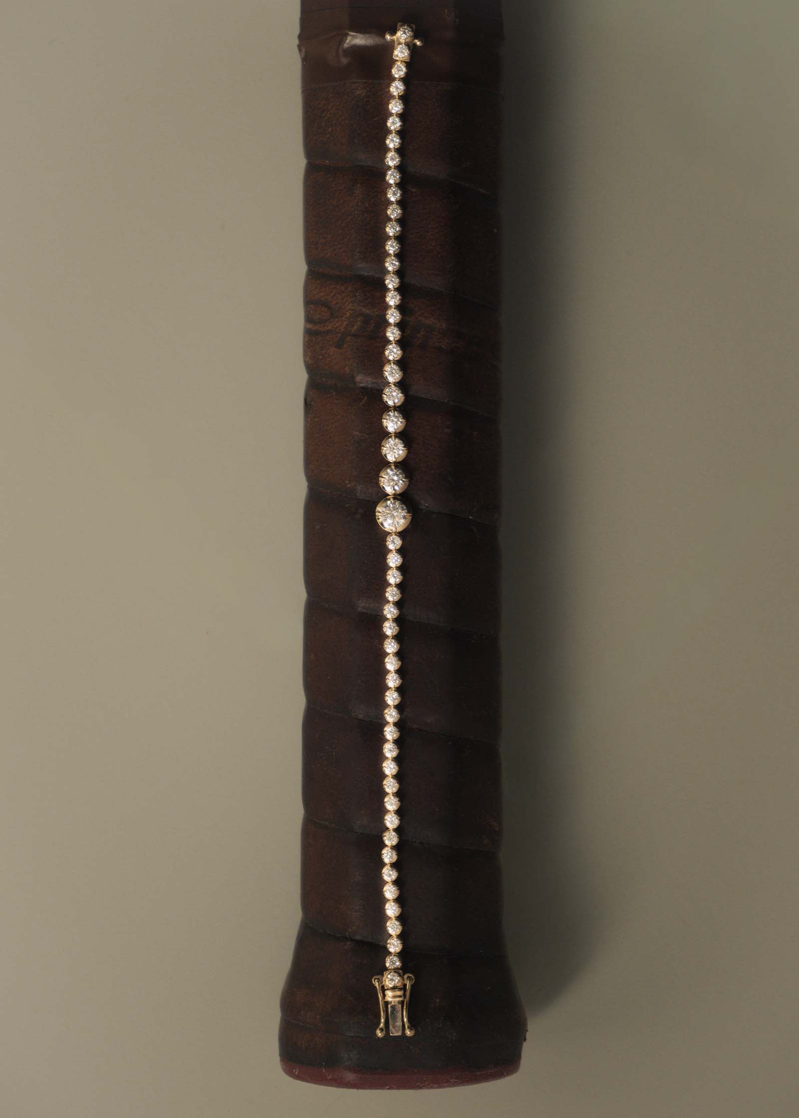 A Kinn x Prince 14k Gold Naomi Graduated Diamond Tennis Bracelet laying flat across the handle of a vintage Prince tennis racquet