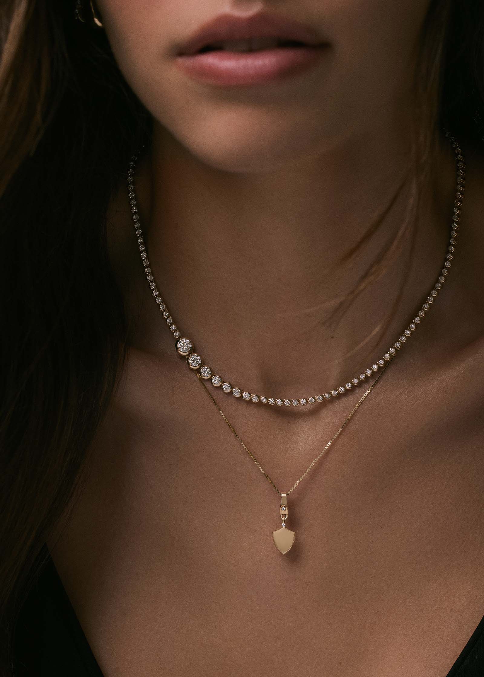 woman wearing a Kinn x Prince 14k Gold Naomi Graduated Diamond Tennis Necklace layered with an Ace Shield Diamond Pendant Necklace on a box chain