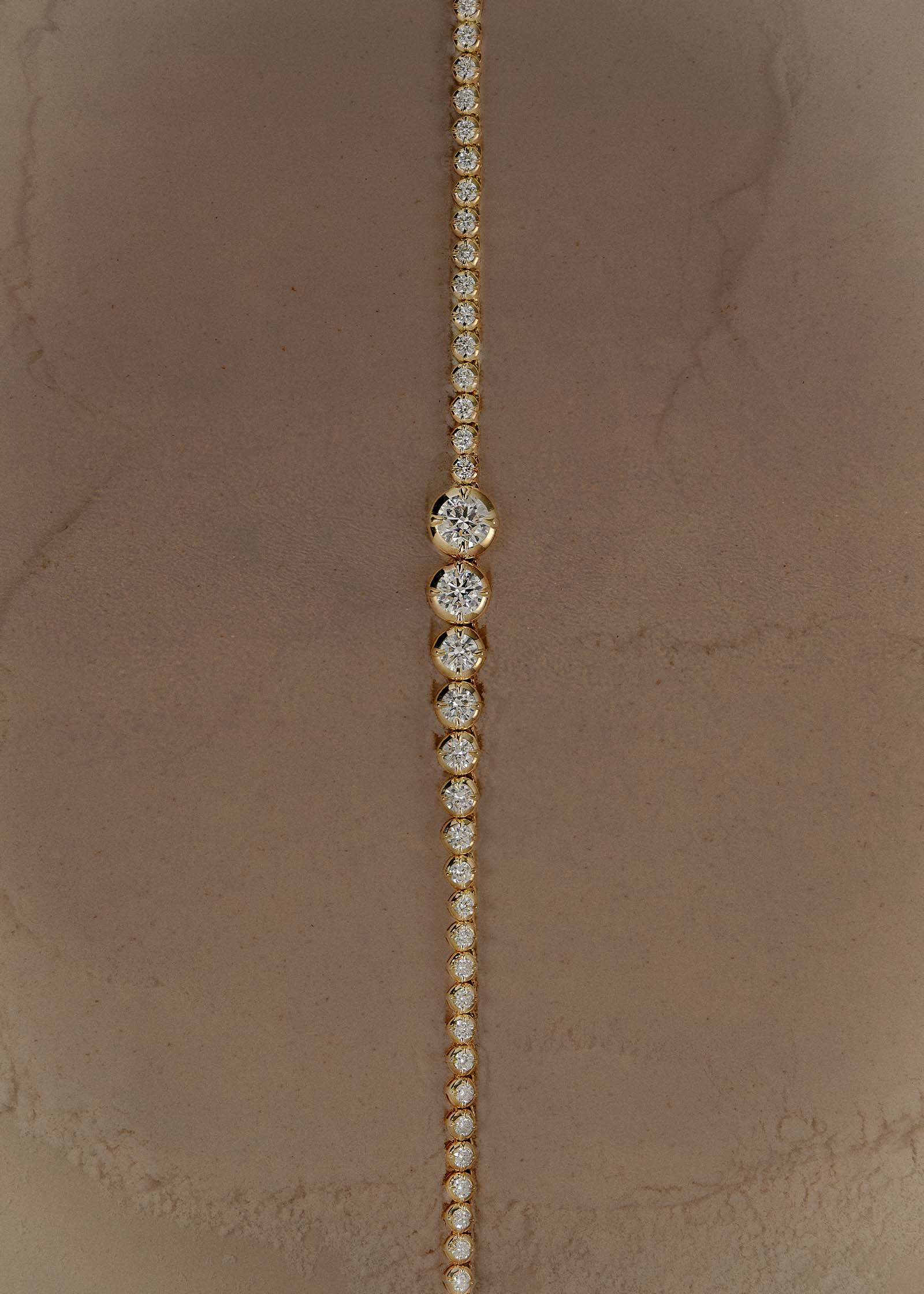 A Kinn x Prince 14k Gold Naomi Graduated Diamond Tennis Necklace laying flat and centered vertically down against a stone background