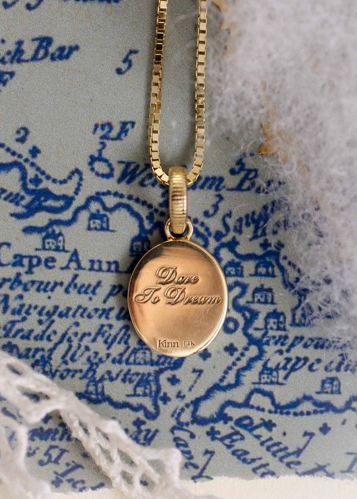 Back of a Kinn 14k Gold Pegasus Dream Diamond Pendant against a blue and white background