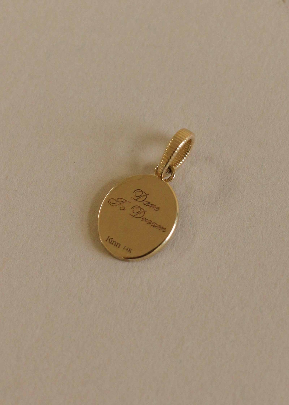 A Kinn 14k Gold Pegasus Dream Diamond Pendant laying flat showing the back engraved with "Dare to Dream"